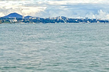 Karadeniz 'in manzarası dağ manzaralı ve ufukta modern bir şehir, bulutlu bir günbatımında