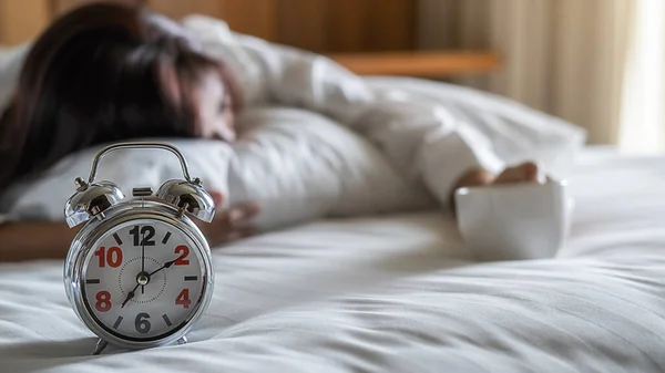 Time to drink coffee. Asian lazy woman lying and holding a cup of coffee on the bed in the morning with soft morning light. Morning lifestyle concept.