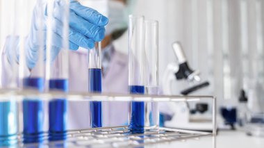 Bilim adamı, ilaç laboratuvarında test tüpü rafında temiz çözeltisi olan bir test tüpü seçiyor. Yenilik Konsepti.