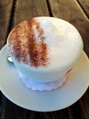 Mükemmel köpüklü bir cappuccino kahve. Bir fincan tabağında servis edilir. Ahşap masa üzerinde..