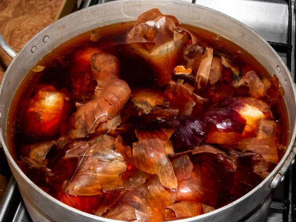 Soğan kabuklarından gelen kahverengi suyla metal tencere farklı yapraklar, bitkiler ve çiçekler kullanılarak boyanmış Paskalya yumurtaları. Ev yapımı geleneksel Paskalya yumurtası renkleri. Soğan kabukları ve derileri. Yukarıdan görüntüle