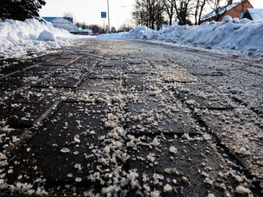 Salt grains on icy sidewalk surface in the winter. Applying salt to keep roads clear and people safe in winter weather from ice or snow, closeup view. clipart