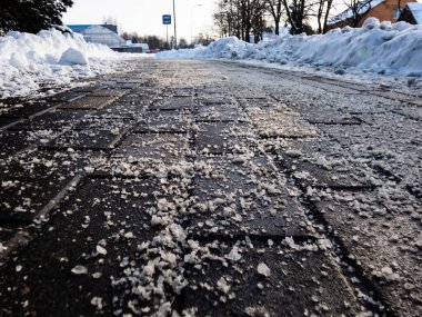 Salt grains on icy sidewalk surface in the winter. Applying salt to keep roads clear and people safe in winter weather from ice or snow, closeup view. clipart