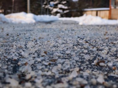 Macro shot of salt grains on icy sidewalk surface in the winter. Applying salt to keep roads clear and people safe in winter weather from ice or snow, closeup view. clipart