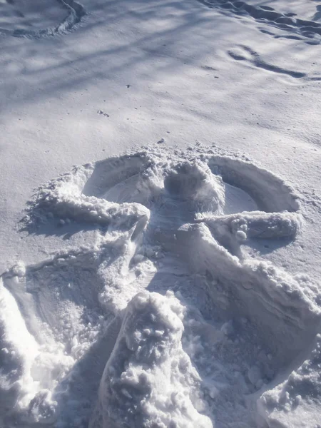 Snow angel design made in fresh, deep snow, by lying on back and moving arms up and down, and legs from side to side in winter on a sunny day