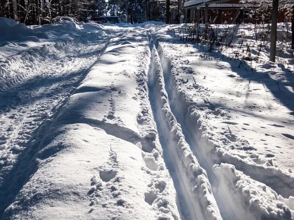 A cross-country ski track forms direct trail that disappears into the distance. The parallel lines of the groomed path, deeply indented ski tracks on a beautiful winter day