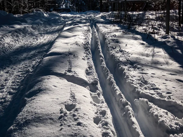 A cross-country ski track forms direct trail that disappears into the distance. The parallel lines of the groomed path, deeply indented ski tracks on a beautiful winter day