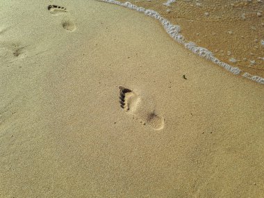 Sarı kumsaldaki insan ayak izleri Baltık kıyısı yakınlarında yalınayak yürürken ayak izlerini suyla silmiş. Hayatın tefekkürü