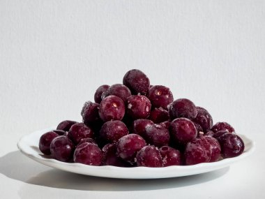 Donmuş, tatlı, olgun kiraz meyveleri beyaz tabakta eriyor ve beyaz bir tabakta eriyor.