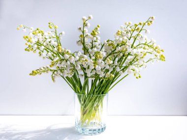 Camdaki vadideki zambak buketi parlak güneş ışığında beyaz arka planda izole edilmiş. Zarif çiçek arkaplanı. Vadi Zambağı 'nın çan şeklinde beyaz çiçekleri (Convallaria majalis))