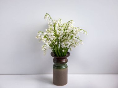 Tatlı kokulu, kolsuz, çan şeklinde, beyaz çiçekli vadi Zambağı (Convallaria majalis) beyaz masa ve arka planda eski, jöleli kil vazo. Zarif çiçek arkaplanı