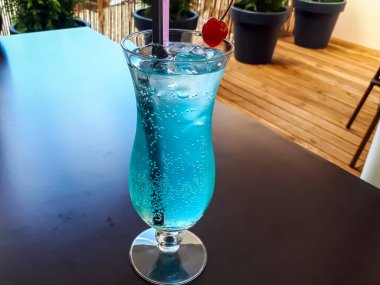 Bir bardak mavi alkollü içecek - Kokteyl 'Garajın önünde seks' (vodka, şeftali likörü, curacao şurubu, sprite) yazın açık bir terasta karanlık bir masada.