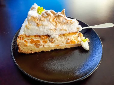 Kremalı, süzme peynirli, şeftalili, kremalı ve koyu renkli bir tabakta caster şekerle süslenmiş üç köşeli tatlı pastası.