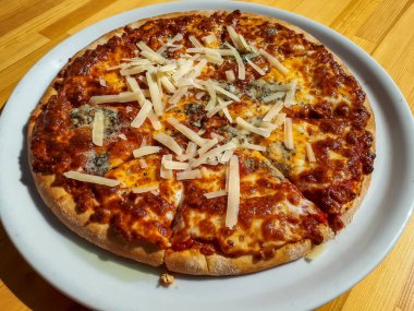 Dört peynirli pizza - domates sosu, mozzarella, gorgonzola, Parmigiano Reggiano, ve keçi peyniri açık havada, ahşap bir masada beyaz bir tabakta, güneş ışığı altında.