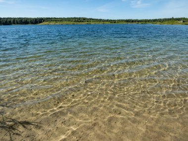 Çok uzaklardaki göl ve ormanın manzarası ve kristal berrak ışık dokusu mavi, yeşil ve turkuaz şeffaf su, ince beyaz kum tabanı ve yazın güneşin parlak yansıması.