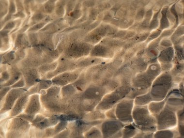 Kristal berrak şeffaf su dokusu, ince beyaz kum tabanı ve su hareketindeki güneşin parlak yansıması.