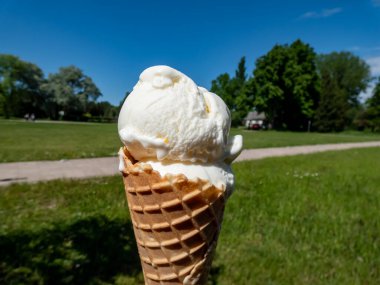Krep külahındaki vanilyalı dondurma topları yeşil manzaralı ve sıcak yaz aylarında mavi gökyüzü arka planında sıcakta erimeye başlar.