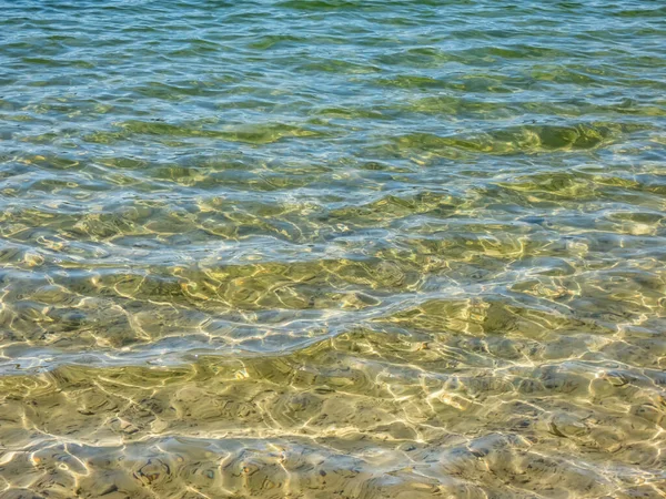 クリスタルクリアライトのテクスチャ水の動きで太陽の明るい反射と細かい白い砂のベースと青 緑とターコイズ透明水 — ストック写真