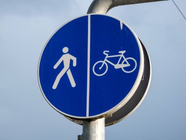 Metal yol işareti (arkadaki mavi gökyüzüne karşı yaya ve döngüsel mavi yuvarlak, bisikletçiler ve yayalar için ayrık yol ve yol anlamına gelir