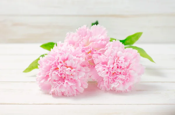 Rosa pastellfarbene künstliche Nelkenblüten auf weißem Holztisch — Stockfoto