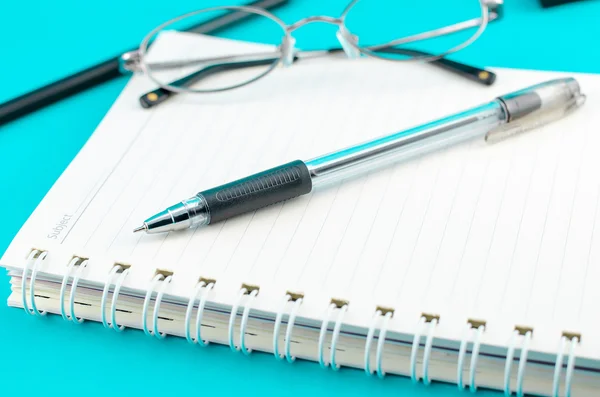 Penna da primo piano con notebook e occhiali su sfondo blu — Foto Stock