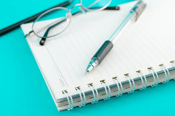 Pluma de primer plano con cuaderno y gafas sobre fondo azul — Foto de Stock