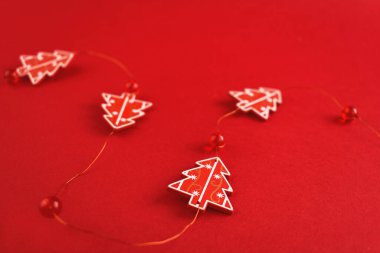 Noel süsü. Kırmızı arkaplanda kırmızı Noel ağaçlarından ve boncuklardan yapılmış bir çelenk. Yeni yıl, Noel konsepti. Noel süslemesi.