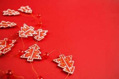 Noel süsü. Kırmızı arkaplanda kırmızı Noel ağaçlarından ve boncuklardan yapılmış bir çelenk. Yeni yıl, Noel konsepti. Noel süslemesi.