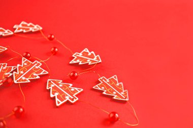 Noel süsü. Kırmızı arkaplanda kırmızı Noel ağaçlarından ve boncuklardan yapılmış bir çelenk. Yeni yıl, Noel konsepti. Noel süslemesi.