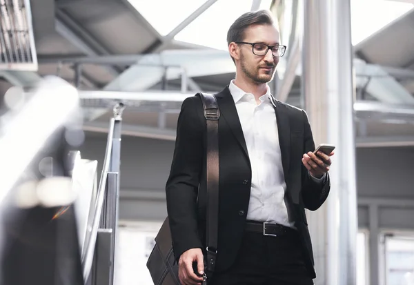 Чоловік на смартфоні - молодий бізнесмен в аеропорту. Красиві чоловіки в окулярах носять куртку в приміщенні — стокове фото
