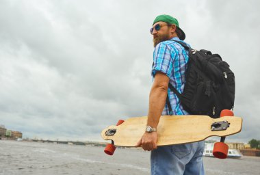 Yakışıklı hipster adam ayağa longboard ile şehir nehir arka plan üzerinde.