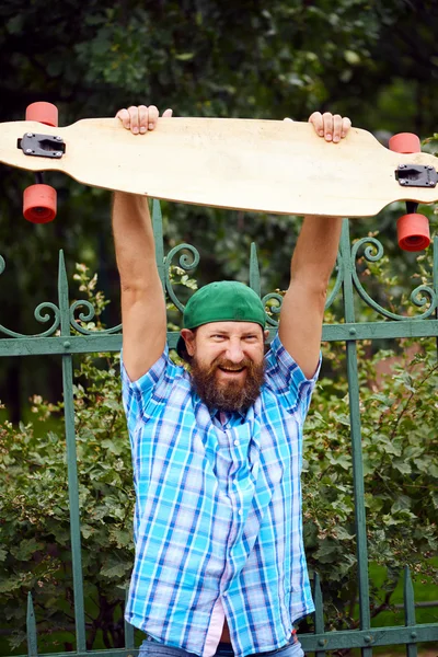 Alegre hipster hombre posando con longboard y en la gorra verde de moda . —  Fotos de Stock