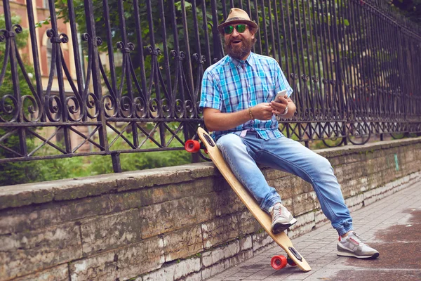 Hipster hombre charlando en el parque con tabla larga. Hombres guapos en gafas de sol y sombrero posando al aire libre —  Fotos de Stock