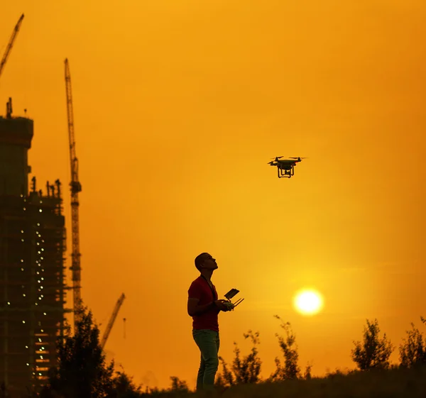 El hombre controla un quadrocopter al atardecer. Edificio nuevo en segundo plano — Foto de Stock