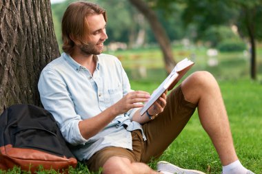 Park kampüs gülümseyen öğrenci bir kitap okumak