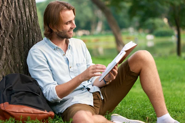 Lächelnder Student im Park des Campus liest ein Buch — Stockfoto