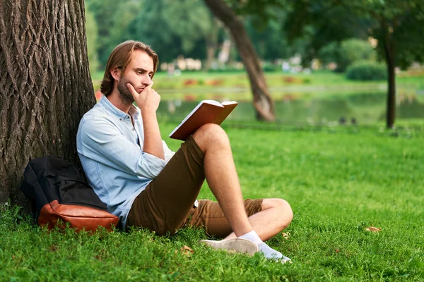 Étudiant sérieux dans le parc du campus lire un livre — Photo