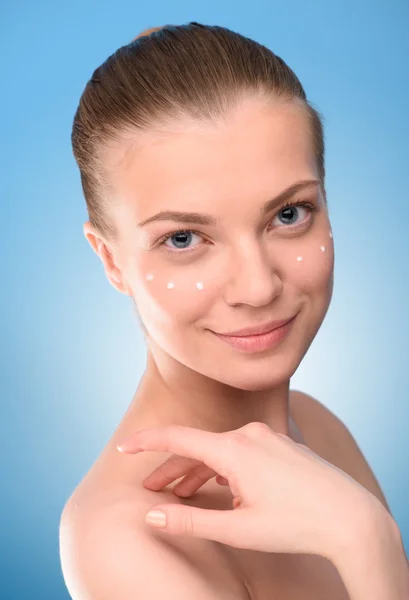 Mujer aplicando crema de elevación en la cara, sobre fondo azul . —  Fotos de Stock