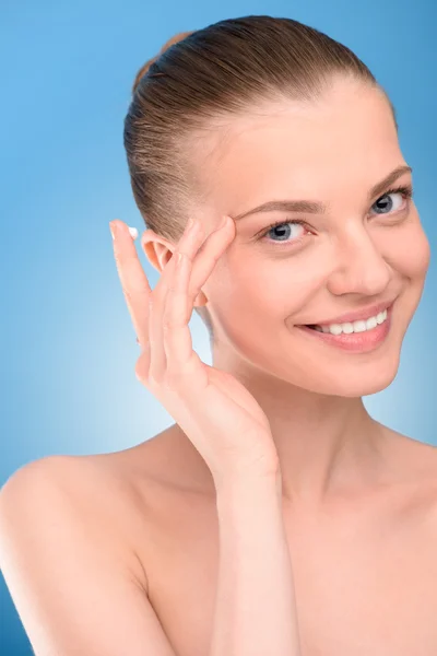 Woman applying lifting cream on face, over blue background. Stock Picture