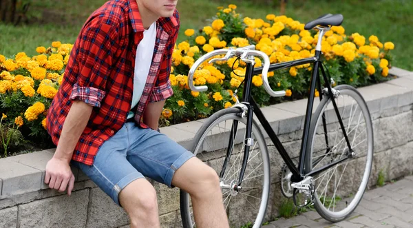 Hipster homem com bicicleta descansando sobre canteiro de flores com flores amarelas — Fotografia de Stock