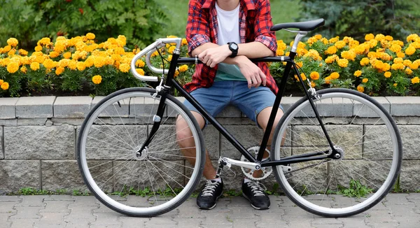 Hipster man med cykel över blomsterrabatt därjämte gula blommor — Stockfoto