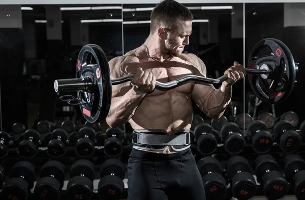 Culturista muscular atleta en el gimnasio entrena bíceps con barra — Foto de Stock