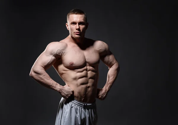 Hombre musculoso en el estudio sobre fondo oscuro muestra su cuerpo — Foto de Stock