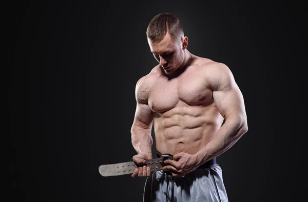 Muscular hombre abrocharse cinturón de elevación posando sobre fondo oscuro — Foto de Stock