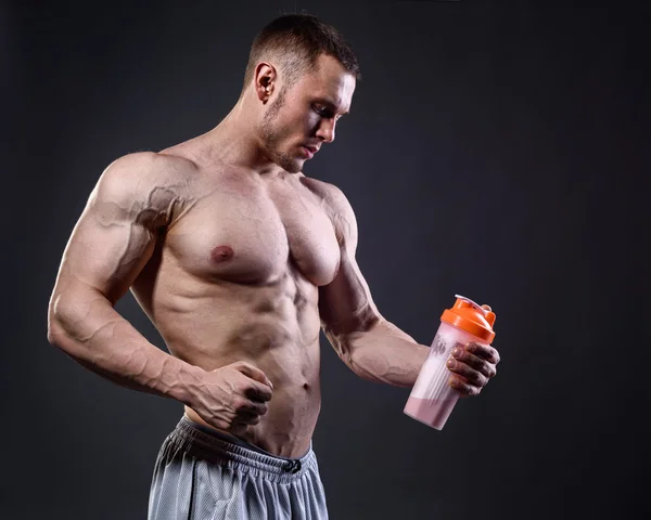 Atleta uomo guardando il frullatore di proteine su sfondo scuro — Foto Stock