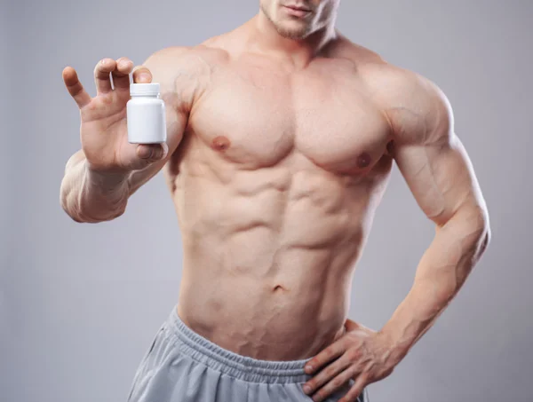 Bodybuilder mit einem weißen Gefäß mit Pillen auf dem Hintergrund. Studioaufnahme — Stockfoto