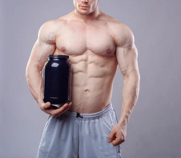 Bodybuilder hält ein schwarzes Plastikgefäß mit Molkenprotein auf grauem Hintergrund — Stockfoto