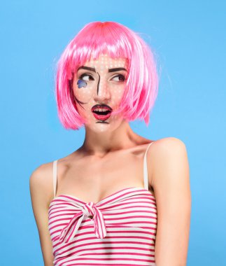 Beauty head shot. Surprised Young woman with creative pop art make up and pink wig looking at the camera on blue background