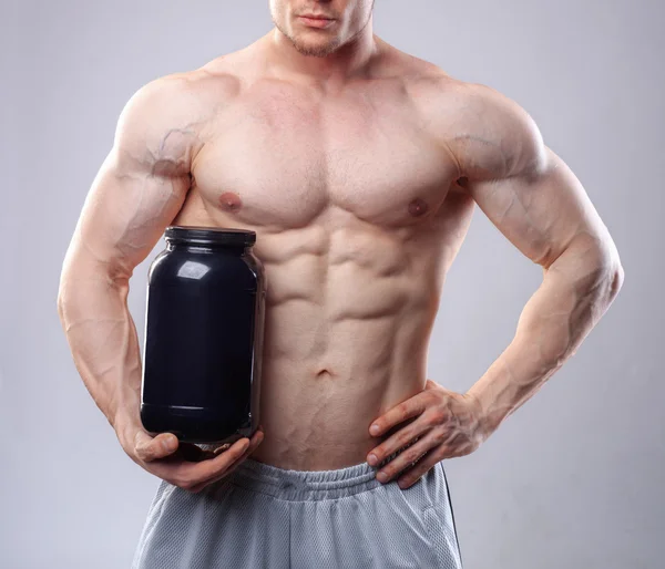 Culturista in possesso di un vaso di plastica nero con proteine del siero di latte su sfondo grigio — Foto Stock