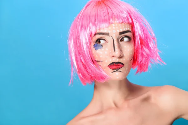 Beauty head shot. Young woman with creative pop art make up and pink wig looking at the camera on blue background